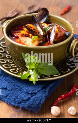 Speisekonzept Thai sauer rot Curry Muscheln Ananas Kang Kua Hoi in grüner Keramikschale auf blauem Serviettenholz Hintergrund Mit Kopierbereich Stockfoto