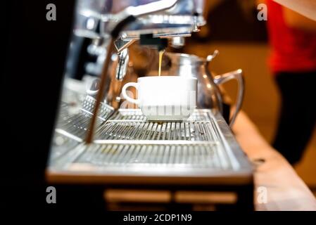 Gefilterter Kaffee fällt aus der Espresso-Mahlmaschine in eine Tasse. Stockfoto