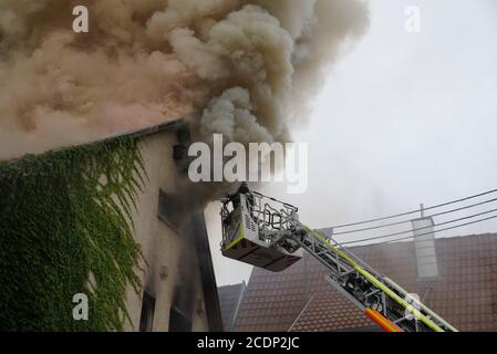 29. August 2020, Baden-Württemberg, Kirchheim unter Teck: Feuerwehrleute versuchen, das Feuer in einem Haus im Landkreis Esslingen zu löschen, aus dem dichter Rauch aufsteigt. Bei dem Wohnungsbrand sind vier Personen verletzt worden, darunter auch ein Feuerwehrmann. Zwei Männer sprangen aus dem Fenster und erlitten schwere Verletzungen. Das Feuer war aus noch unbekannten Gründen im zweiten Stock des Wohnhauses ausgebrochen. Die Feuerwehrleute kamen am Samstagmorgen an und waren immer noch damit beschäftigt, das Feuer am Morgen zu löschen. Laut Polizei ist das Gebäude nicht mehr bewohnbar. Foto: Kohls/SDMG Stockfoto