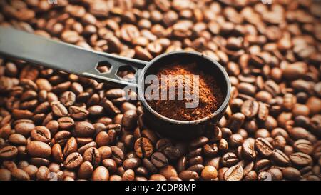 Ein langer, schwarzer, eleganter Messlöffel mit gemahlenem Kaffee liegt auf den gerösteten, aromatischen Kaffeebohnen, aus denen er hergestellt wird. Stockfoto