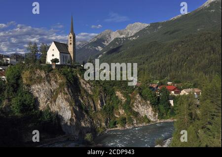 Spätgotische, reformierte Kirche St. George, auf einer Klippe über dem River Inn, in Scuol im unteren Engadintal, Graubünden oder Grisons Kanton, Schweiz. Die Kirche wurde 1516 geweiht, hat aber einen romanischen Turm, der von einer früheren Kirche überlebt hat. Stockfoto