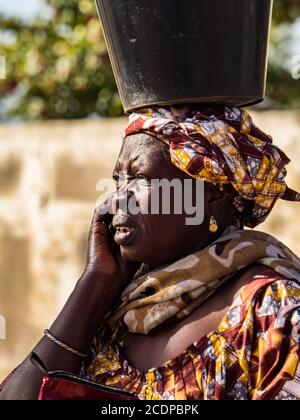 Joal-Fadiouth, Afrika - Jan, 2019: Senegalesische Frau mit einem Eimer auf dem Kopf. Die Region Thiès am Ende der Petite Côte von Senegal Stockfoto