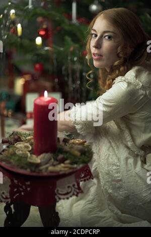 Viktorianisch scheinende Weihnachtsszene mit jungen rothaarigen Frau in einem Antik-Kleid mit Kerze Stockfoto