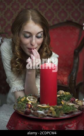 Viktorianisch scheinende Weihnachtsszene mit jungen rothaarigen Frau in einem Antik-Kleid mit Kerze Stockfoto