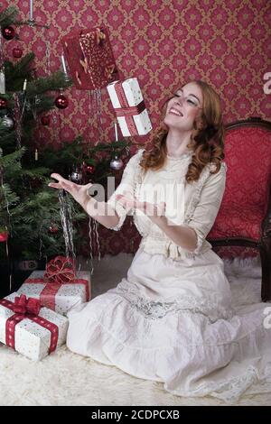 Viktorianisch scheinende Weihnachtsszene mit jungen rothaarigen Frau in einem Antik-Kleid mit Geschenk Stockfoto