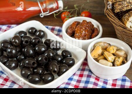 Schwarze Oliven, sonnengetrocknete Tomaten und Muscheln in Keramikschalen Stockfoto