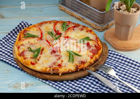 Traditionelle hawaiianische Pizza auf einem Holztablett auf dem Tisch mit karierter Serviette. Runde Pizza mit Fleisch, Pfeffer, Wurst, Rosmarin und Käse Stockfoto