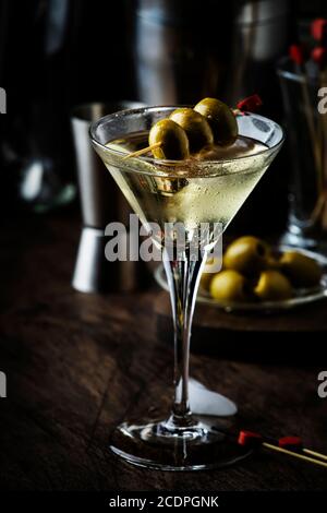 Martini-Cocktail, mit trockenem Wermut, Wodka und grünen Oliven, Bar-Theke aus Vintage-Holz mit Bar-Werkzeugen Stockfoto