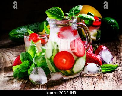 Gurken-Basilikum-Limonade mit Erdbeeren und Eis in einem Krug, Vintage-Holzhintergrund, selektiver Fokus Stockfoto