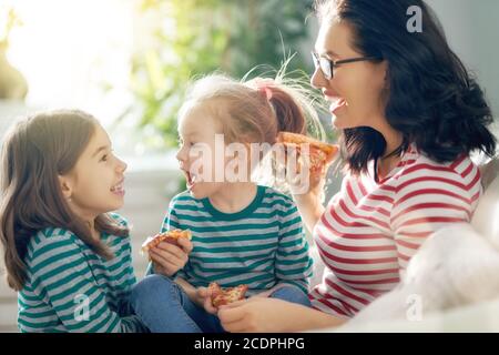 Glückliche liebevolle Familie. Mutter und ihre Töchter Kinder Mädchen essen Pizza auf dem Sofa im Zimmer. Stockfoto