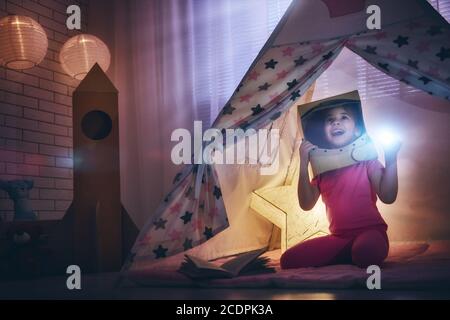 Kind in einem Astronauten Kostüm mit Spielzeug Rakete spielen und träumen von einem Raumfahrer zu werden. Glückliches Kind spielt im Zelt. Lustige schöne Mädchen mit Spaß in ch Stockfoto
