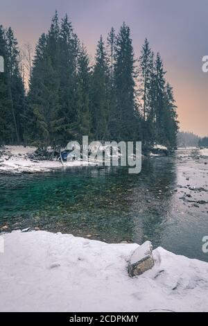 Sonnenuntergang über verschneiten Fluss und Wald in der Tatra, Polen Stockfoto