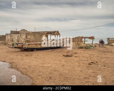 Nianing, Senegal - 24. Januar 2019: Zerstörte hölzerne Fischerboote stehen an einem Sandstrand vor einem verlassenen Haus in Ruinen. Afrika Stockfoto