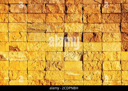 Wand mit beigefügten gelben ungleichmäßigen strukturierten Ziegelsteinen stehen vor einem sehr warmen goldenen Licht. Es hat einen dreidimensionalen Look. Stockfoto