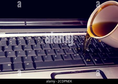 Kaffee wird aus einer Tasse auf den Laptop gegossen Stockfoto