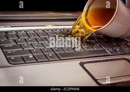 Kaffee wird aus einer Tasse auf den Laptop gegossen Stockfoto