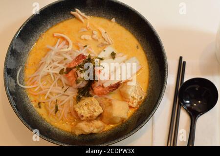 Draufsicht auf eine Schüssel mit Laksa mit Löffel und Essstäbchen. Laksa ist eine typische Suppe aus Südostasien Stockfoto