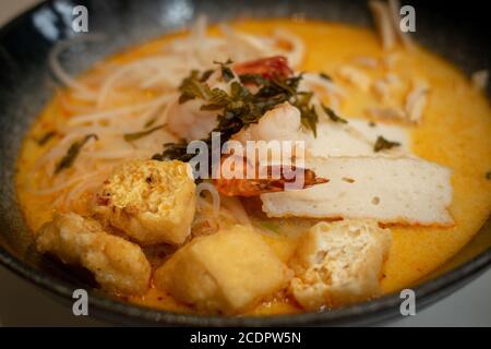 Eine Schüssel Laksa, typische Suppe aus Südost-Asian, die aus Weizennudeln, Huhn, Garnelen und Fisch besteht, serviert in würzigem Curry Kokosmilch Stockfoto