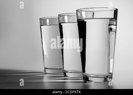 Drei Gläser Wasser auf einem schlichten weißen Hintergrund mit Schatten werfen sich über den Vordergrund Stockfoto