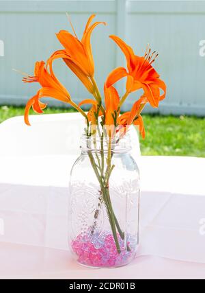 Herzstück von orangen Tigerlilien in einem Glas mit lila Steinen auf einem Tisch in einem Hinterhof für eine Veranstaltung. Stockfoto