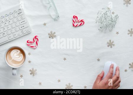 Weiß-Stil Draufsicht, Computer-Arbeitsplatz und weibliche Hand auf Maus. Winterzeit flach legen mit Kaffeetasse, Herzen aus Süßigkeiten Stöcke, Papier Konfetti, Schneef Stockfoto