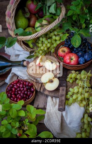 Stillleben im Herbst. Früchte und Beeren. Äpfel, Trauben, Erdbeeren, Pflaumen auf einem Holztisch. Landhausstil. Leere gesunde Vitaminnahrung. Obsternte. Stockfoto