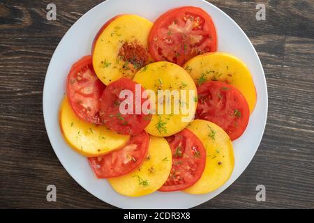 Farbenfroher Sommersalat mit Tomaten und Nektarinen, gewürzt mit einer Sauce aus Olivenöl, Zitronensaft und Balsamico-Essig, Nahaufnahme Stockfoto