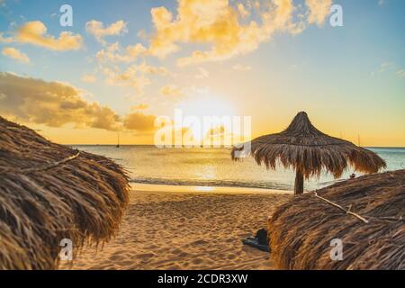 Heller Sonnenuntergang an einem Ferienstrand mit Strohtikis und Sand Stockfoto