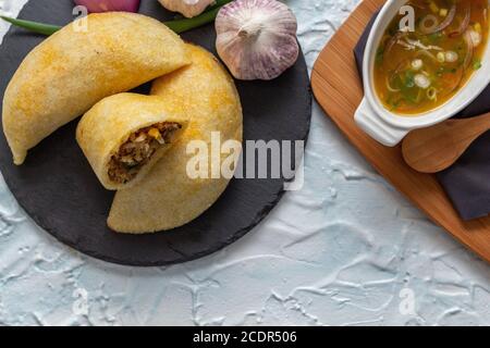 Foto von oben von kolumbianischen Empanadas mit etwas Chili Paprika serviert auf einem schwarzen rustikalen Teller. Sie werden mit Maismehl gemacht und gefüllt Stockfoto