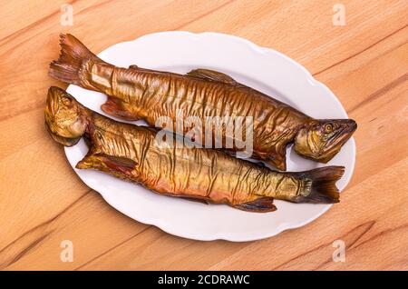 Zwei geräucherte Fische, Bachforelle, auf einem weißen Teller auf einem Buchentisch. Stockfoto