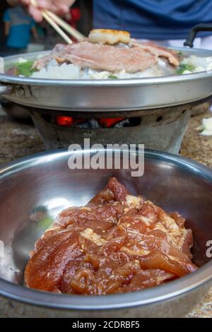 Ein rohes Schweinefleisch in einer Schüssel bereit zum Grillen bei Thai Barbecue Stil. Eine Zubereitung von gebratenem Fleisch mit Gemüsesauce auf Hot Pot - Mu Kratha, close up Stockfoto