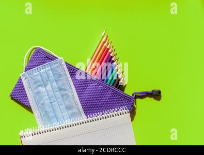 Bunt gefärbtes Bild mit Kinderkoffer, Buntstiften, Schulheft und Maske gegen Covid 19 Stockfoto