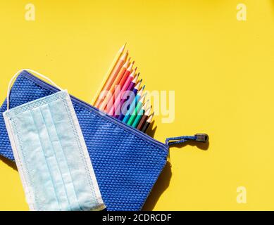 Buntes Bild mit Kinderkoffer, Farbstifte und Maske gegen Covid 19. Zurück zur Schule Stockfoto