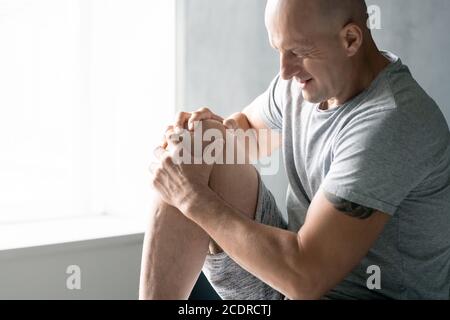 Zeitgenössische Glatze reifen Sportler in activewear massiert sein rechtes Knie Stockfoto