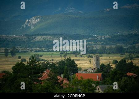 Ein kleines Dorf mit vielen verlassenen Häusern und einem alten Kirchturm liegt auf Ebenen in der Nähe von Ausläufern. Stockfoto