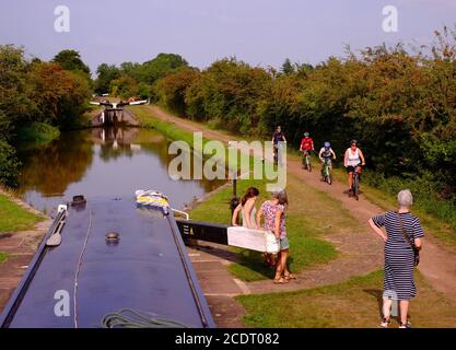 Leben auf dem Worcester und Birmingham Canal als Familie Radfahren auf dem Treidelpfad vorbei an einem schmalen Boot durch eine Schleuse. Stockfoto