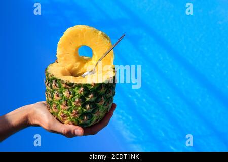 Hand hält frische Ananas über dem blauen Swimmingpool Stockfoto