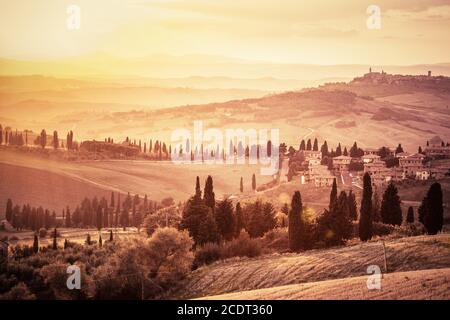 Wunderschöne toskanische Landschaft mit Zypressen, Bauernhöfen und kleinen mittelalterlichen Städten, Italien. Sonnenuntergang im Vintage-Stil Stockfoto