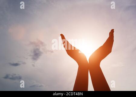 Erhöhte Hände fangen Sonne auf Sonnenuntergang Himmel. Konzept von Spiritualität, Wohlbefinden, positive Energie Stockfoto