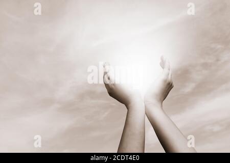 Erhöhte Hände fangen Sonne auf bewölktem Himmel. Konzept von Spiritualität, Wohlbefinden, positive Energie Stockfoto