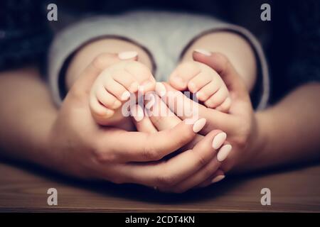 Kleine Babyfüße in den Händen der Mutter. Kinderbetreuung, sich sicher fühlen, schützen. Stockfoto