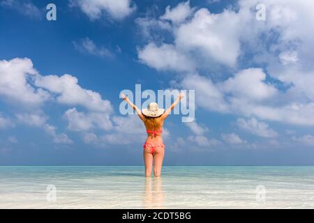 Schöne junge Frau, die im Meer mit erhobenen Händen steht. Malediven Stockfoto