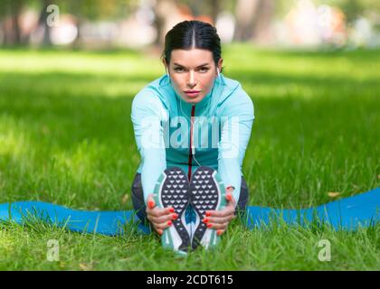 Frau erwärmt Muskeln vor dem Joggen. Sitzen auf Gras im Stadtpark - Frau dehnende Muskeln. Nahaufnahme. Stockfoto