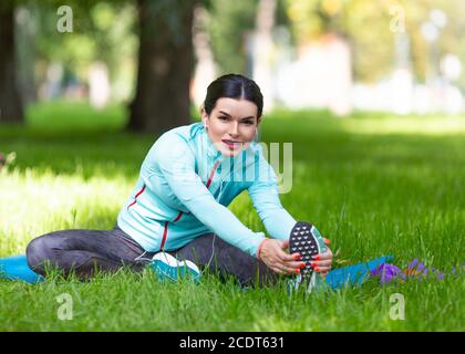 Frau erwärmt Muskeln vor dem Joggen. Sitzen auf Gras im Stadtpark - Frau dehnende Muskeln. Stockfoto