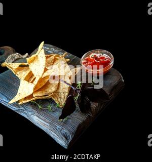 Nachos auf Holzuntergrund mit Basilikum und Thymiansoße und Kräutern. Isoliert auf Schwarz Stockfoto