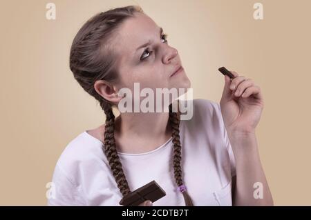 Das Mädchen schmeckt Schokolade. Das Mädchen genießt den Geschmack von Schokolade. Genießen Sie den Geschmack von Schokolade. Chocolate Day. Süßigkeiten Tag. Das Mädchen wird erschossen Stockfoto