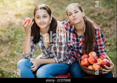 Teenager Mädchen pflücken reife Bio-Äpfel auf dem Bauernhof am Herbsttag. Schwestern mit Obst im Korb. Erntekonzept im Land. Garten, Teenager essen Obst Stockfoto