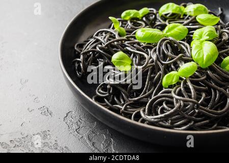 Schwarze Pasta Spaghetti Tintenfisch Tinte mit Basilikumblättern auf schwarzem Hintergrund. Draufsicht. Leerzeichen für Text. Stockfoto