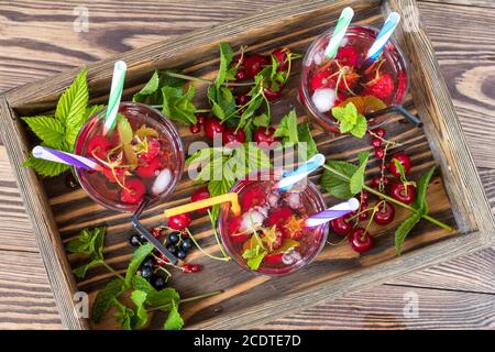 Drei Gläser erfrischenden Drink gewürzt mit frischem Obst im Holzkasten von Obst umgeben. Ansicht von oben. Holz- Hintergrund Stockfoto