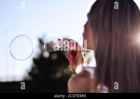 Nette Frau bläst Seifenblasen im Freien im Park am Sommer Sonnenuntergang. Glück in der Natur Konzept. Nahaufnahme, selektiver Fokus Stockfoto